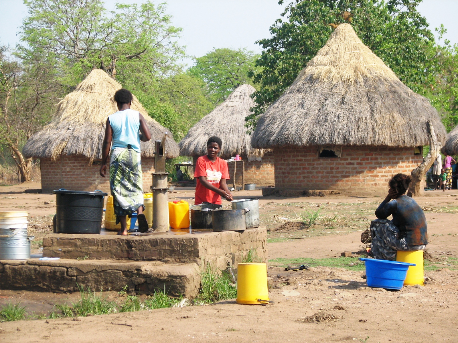 Frauen schöpfen Wasser an einem Brunnen in Sambia und füllen Kanister