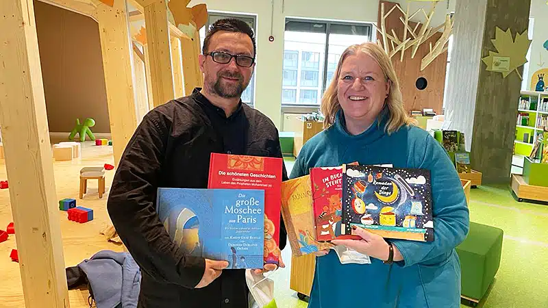 Zwei Personen halten Kinderbücher des Astrolab Verlags in einer Kinderbibliothek in die Kamera