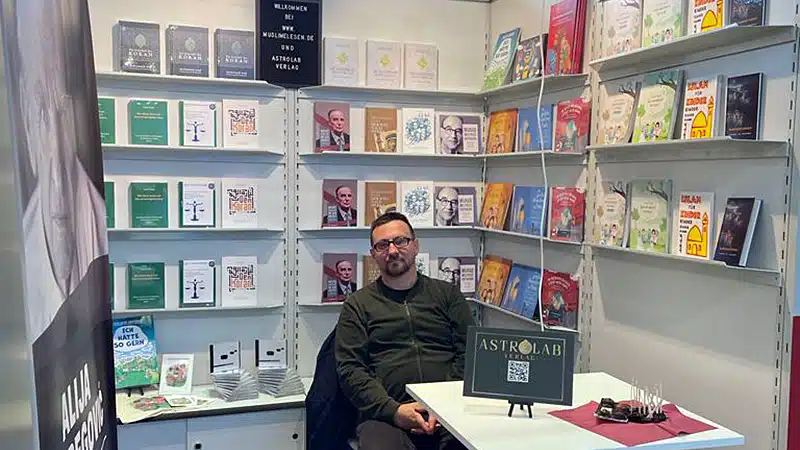 Der Verleger am Messestand des Astrolab Verlags vor Regalen voller Bücher